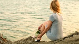 stock-footage-young-woman-sitting-near-a-lake-with-a-bouquet-of-lilies-of-the-valley-in-his-hand